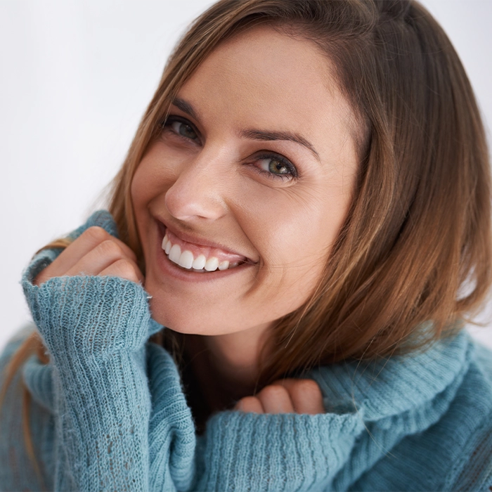A woman wearing a blue sweater smiles warmly at the camera, showcasing natural beauty after a mini facelift in Beverly Hills.