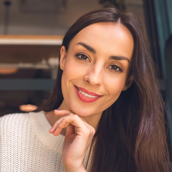 Smiling woman with long brown hair wearing a white sweater, showcasing natural beauty after a mini facelift