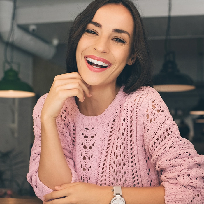 Smiling woman seated at a table, radiating warmth and confidence, representing positive results from a rhinoplasty procedure.