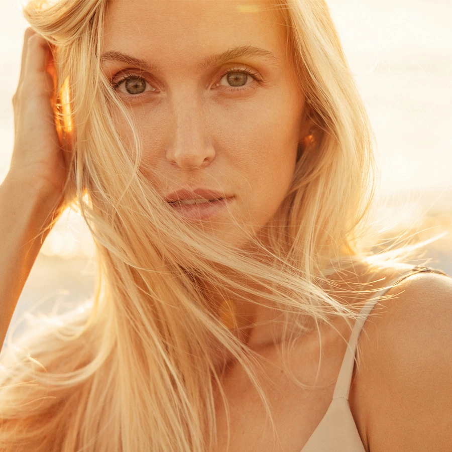 A tight close-up portrait of a woman with light blonde hair and green eyes. Her hair is blowing softly across her face in bright, golden sunlight, creating a warm and airy feel. - Corner of mouth lift in Beverly Hills, CA